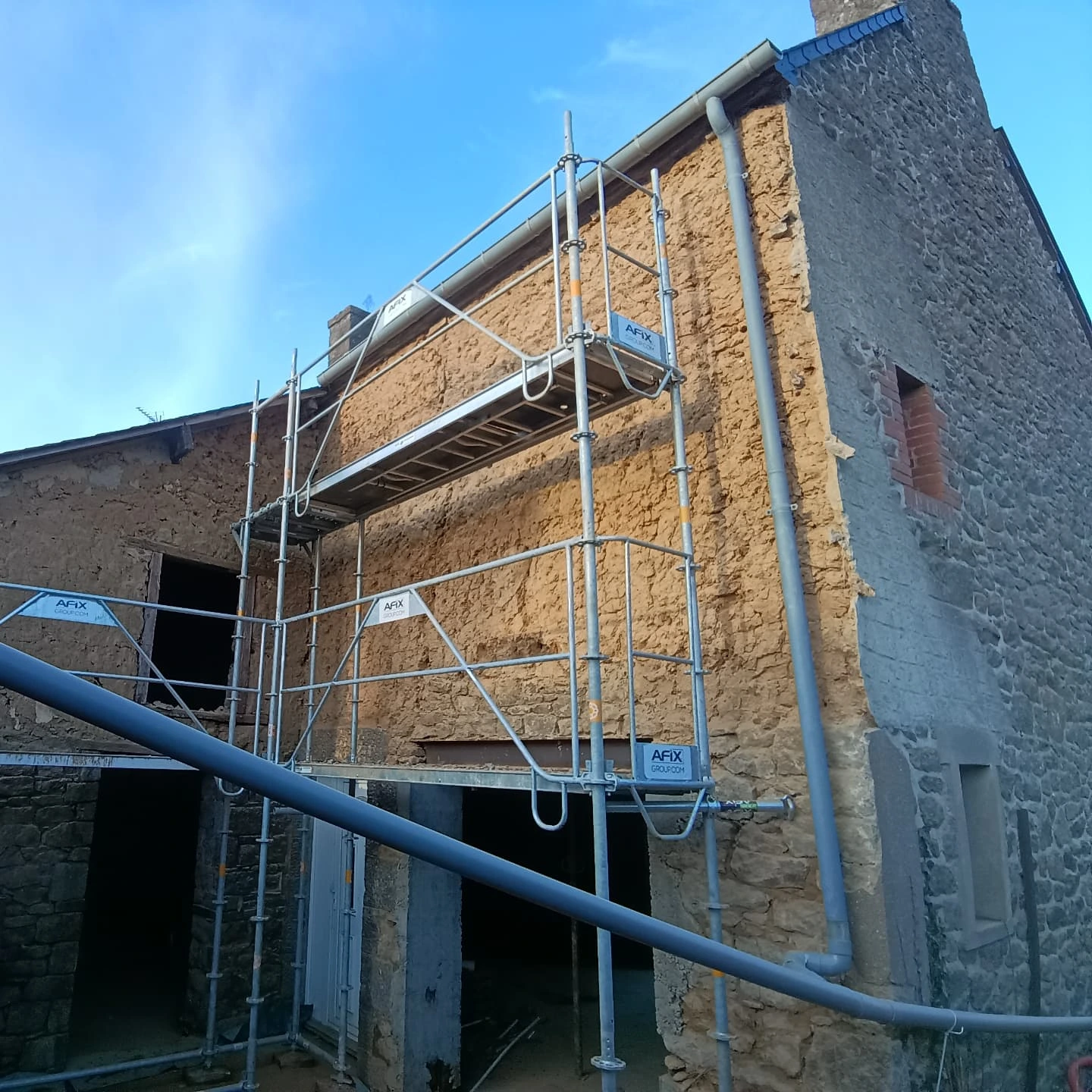 Façade en bauge décapée, échafaudage monté sur un chantier de restauration